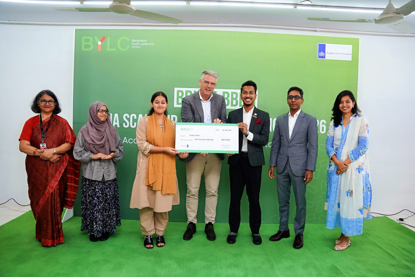 Seven people at a BYLC ceremony hold a large ceremonial cheque for BDT 50,000 made out to Project Utsho