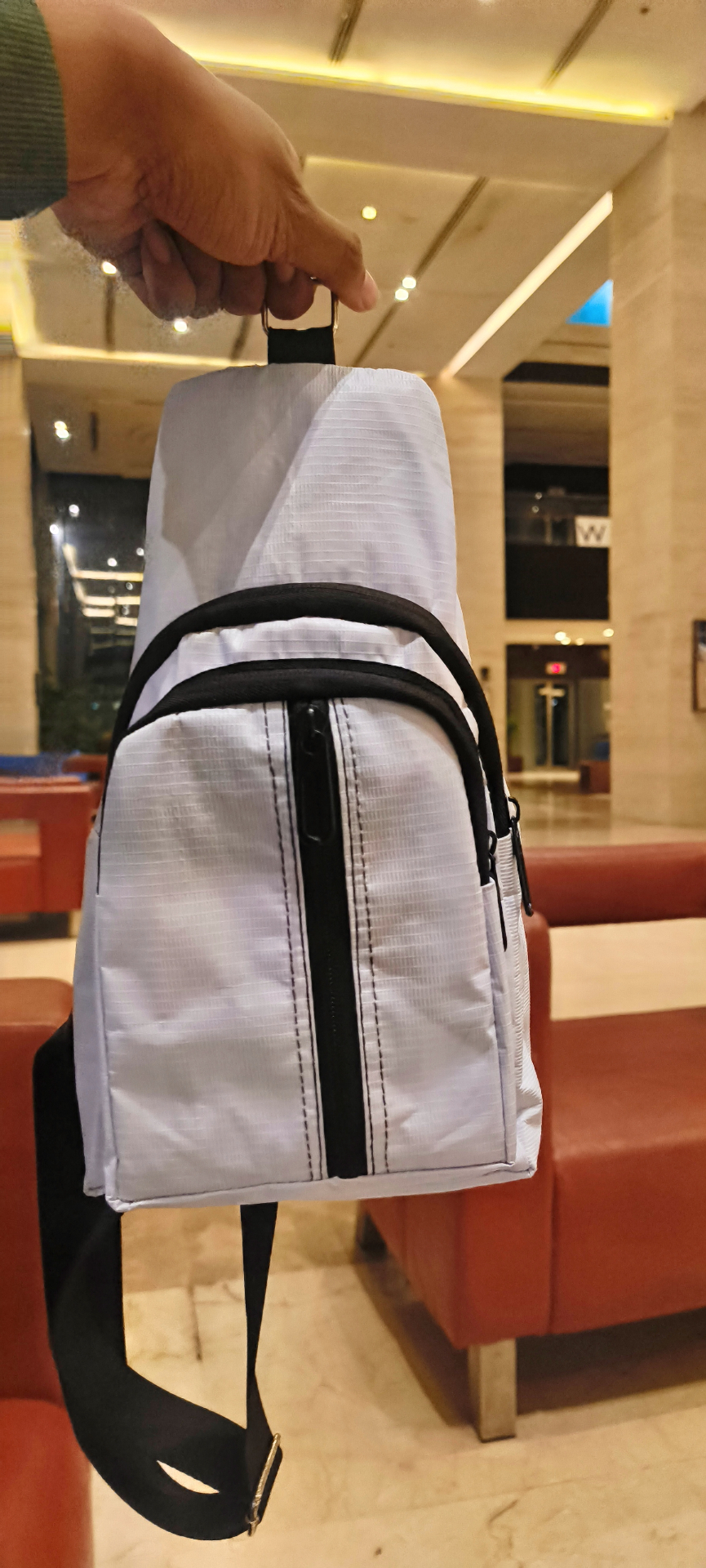 White UTSHO Loop I crossbody bag held up, showing the straight zip down the middle of the front