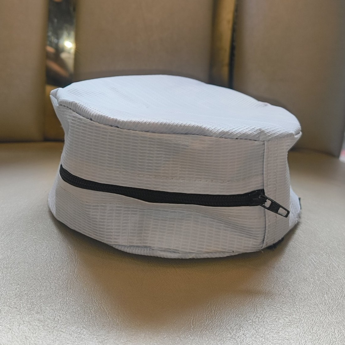 White UTSHO Loop C round arm bag with a black zip, resting on a seat