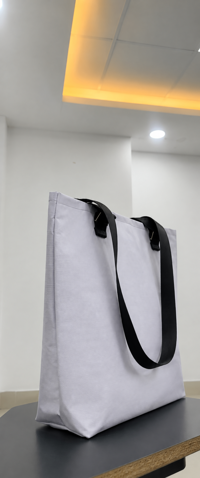 White UTSHO Loop O tote bag with black handles, standing upright on a table