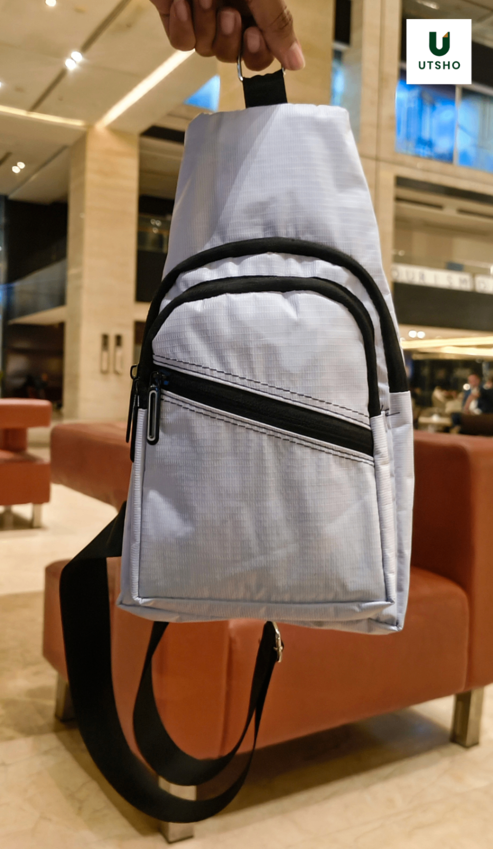 White UTSHO Loop X crossbody bag held up, showing the diagonal zip across the front